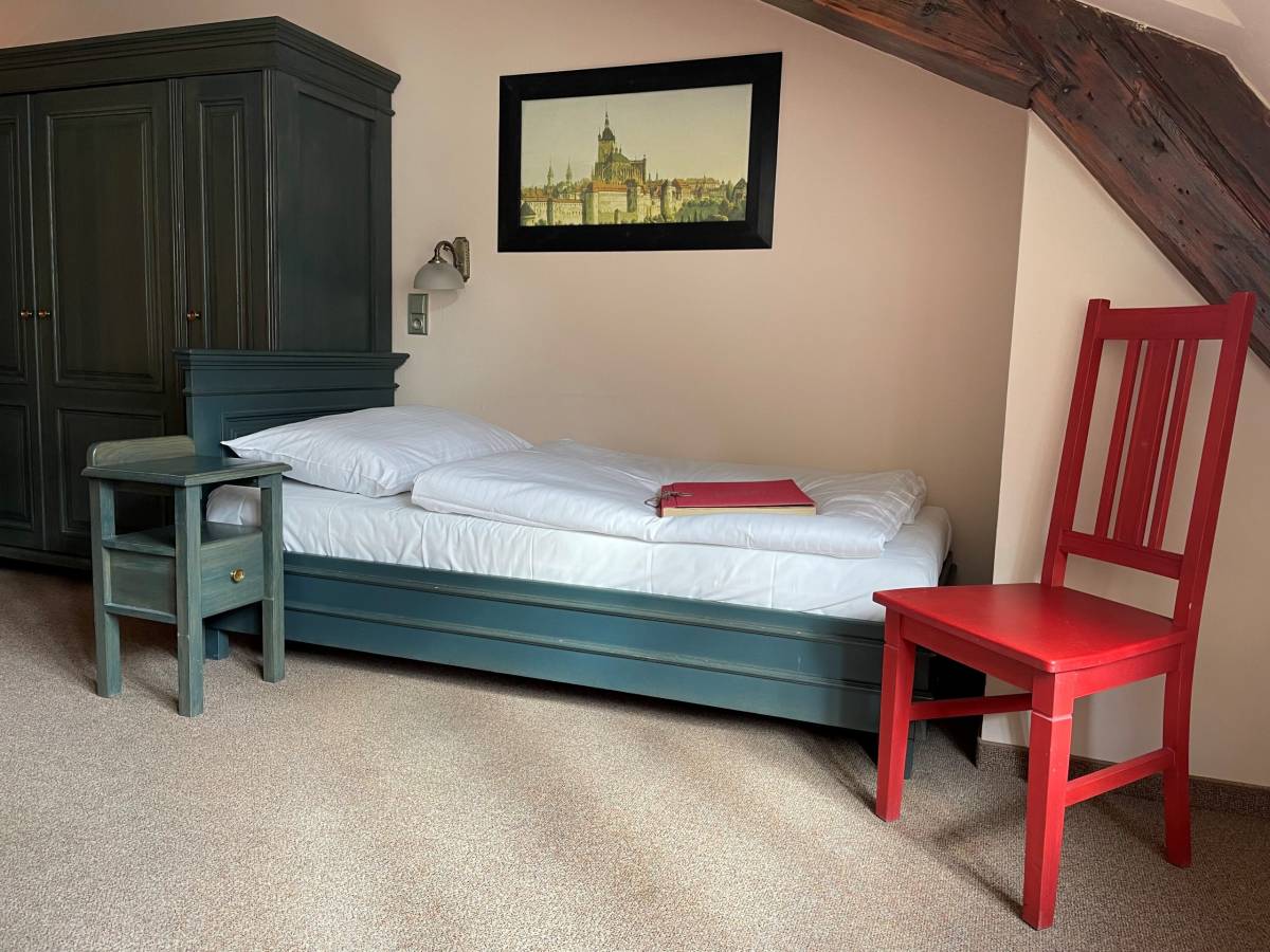 Samostatná postel s konferenčním stolkem, červenou židlí a šatní skříní